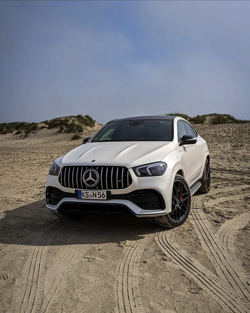 Frontansicht eines weißen Mercedes-AMG GLE 53 Coupé C167 auf Sand mit Panamericana Grill und AMG Styling.