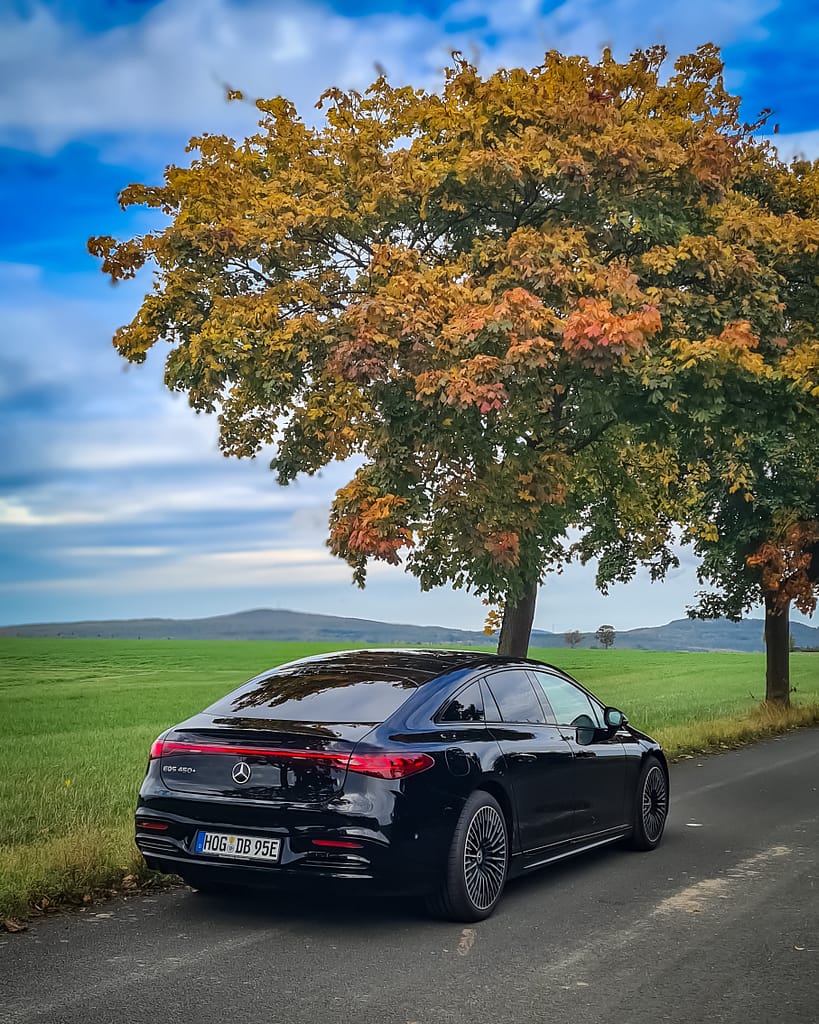 Mercedes-Benz EQS 450+ Heckansicht auf Landstraße unter Herbstbaum