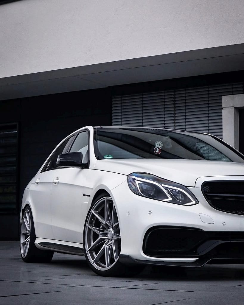 Detailaufnahme eines weißen Mercedes-Benz E63 AMG W212 mit großen silbernen Felgen und schwarzer AMG Frontschürze